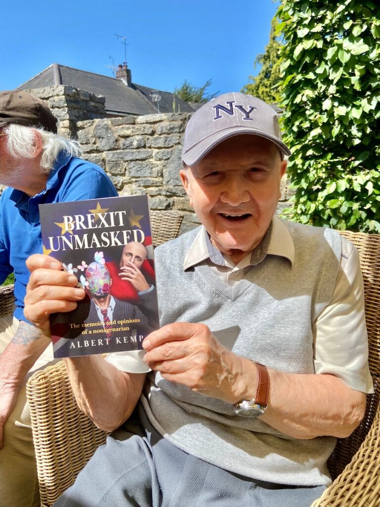 Albert Kemp sitting and holding a copy of his book, Brexit Unmasked.